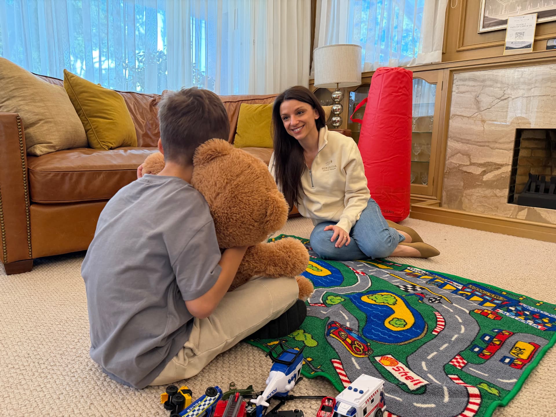 A child holding a teddy bear while talking with a therapist in a welcoming play space